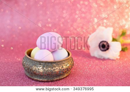 Multi-colored Purple Easter Eggs In A Carved Ceramic Box, White Anemone Flower On A Pink Shiny Bokeh