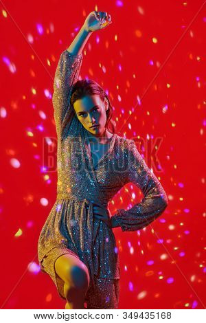 Make-up and cosmetics. Portrait of a gorgeous young woman with golden make-up posing in a colored lights on red background. Party style. 