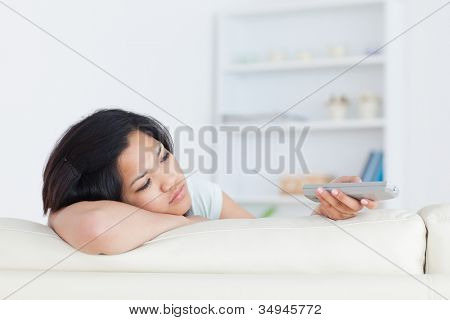 Donna come lei si siede sul divano e detiene un telecomando in un soggiorno di riposo la testa sul suo braccio