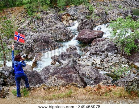 Tourist Woman With Norwegian Flag And Camera Walking Trough Mountains Path In Allmannajuvet Area Sau