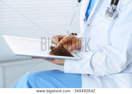 Woman Doctor Using White Tablet Computer While Sitting At Chair In Hospital, Close-up