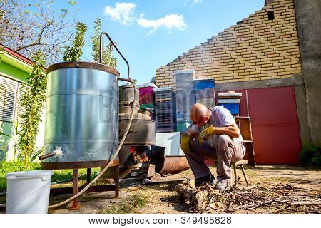 Man Throws Dry Branches Into The Firebox Of A Homemade Distillery Making Moonshine Schnapps, Alcohol