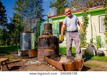 Man Is Manually Turning Lever To Mix Fruit Marc In Boiler Of Homemade Distillery Made Of Copper, Mak