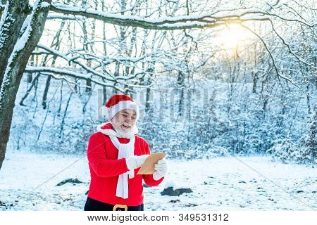 Santa Claus Comes With Gifts From The Outside. Winter Park Trees Covered With Snow. Real Santa Claus