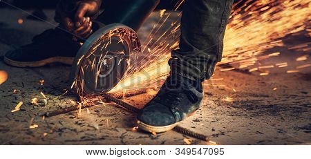 Welder in action, close up photo of hot bright sparks that fly out from under the saw, portable steel cutting machine, hard work, necessary occupation, blue-collar worker, panoramic photo format