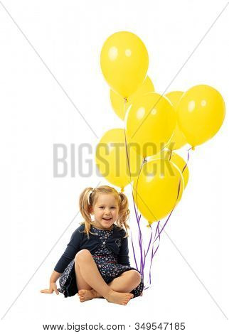 smiling 3 year old Caucasian girl with pigtails holding yellow balloons. isolated on white. concept of happiness and lightheartedness.