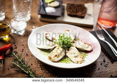 Cooked green mussels with parmegano and cream cheese served on white plate in restaurant