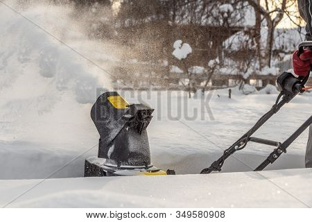 Man Is Brushing White Snow With The Yellow Electric Snow Thrower In A Winter Garden