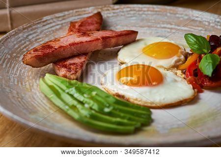 Plate Of Fried Eggs With Bacon And Avocad On Wooden Table. English Breakfast On Table