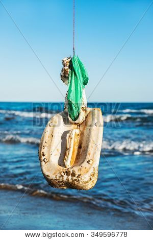 closeup of some used plastic objects in a fish hook, freshly fished in the ocean, in front of the water