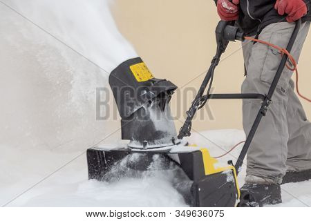 Man Is Brushing White Snow With The Yellow Electric Snow Thrower In A Winter Garden