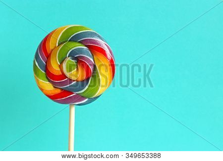 Close-up Of A Multi Colored Lollipop In Rainbow Colors In Front Of A Turquoise Colored Background Wi