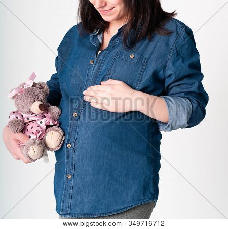 Cropped View Of Pregnant Woman In Blue Shirt Holding Brown Taddy Bear Toy In Pink Dress And Touching