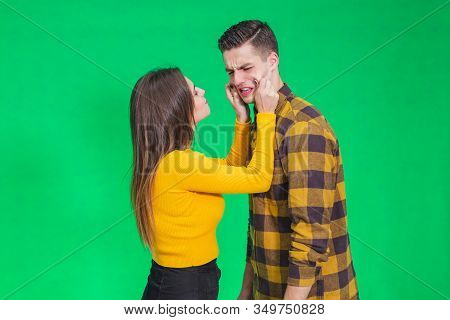 Girl Pinching Guys Cheeks, Making Fyn, He Is Scowling His Face, Looking Completely Annoyed.