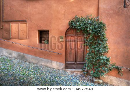 Holztür, kleines Fenster im Haus mit Rost Wand auf kleinen asphaltierten Straße in Saluzzo, nördlichen es
