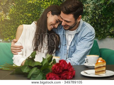 Lovely Couple Hugging Having Romantic Date Sitting In Cozy Cafe Enjoying Coffee And Desserts. Love A
