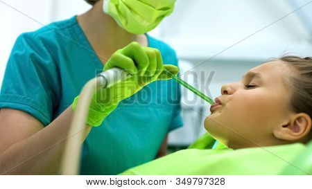 Female Dentist Using Saliva Ejector, Teenage Girl Sitting In Chair Frowning