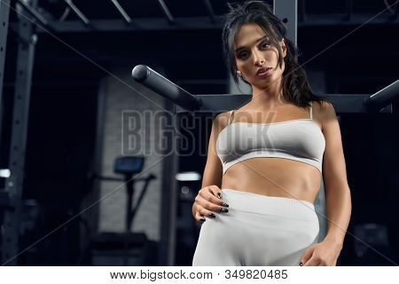 Close Up Portrait Of Female Bodybuilder In Beige Sportswear Posing Near Parallel Bars And Looking At