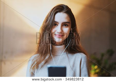 Beautiful Girl Listening To Music In Earphones. Young Female Model With Long Hair And Pretty Face Po