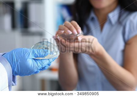 Clinic Visit And Female Breast Implant Selection. Close-up, Doctors Hands In Gloves Holding Female B