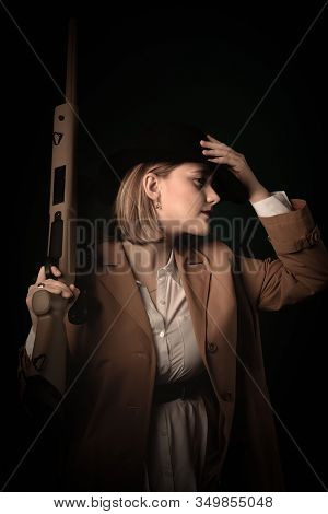 Retro Gangster Woman In A Brown Cloak And Black Hat With Airguns In Hands. Photoshoot In The Style O