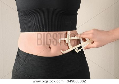 Nutritionist Measuring Woman's Body Fat Layer With Caliper On Beige Background, Closeup