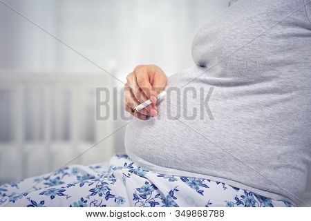 A Pregnant Woman With A Cigarette In Her Hands. Hand And Belly Close-up. The Concept Of Nicotine Add