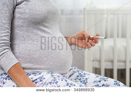 Pregnant Woman With A Cigarette In Her Hands. Hands With A Cigarette And Stomach Close-up. The Conce