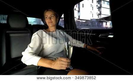 Tired Woman Drinking Champagne On Car Backseat, Driving Home With Private Driver