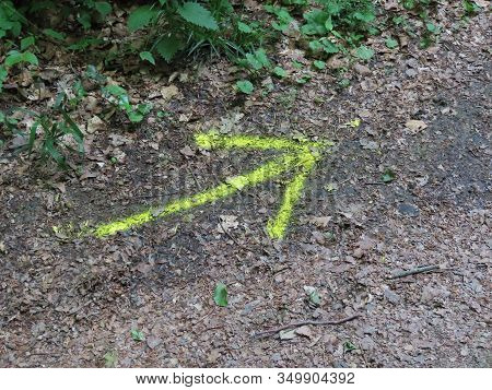 Bright Yellow Arrow Drawn On The Ground: Camino De Santiago Marking In Luxembourg, Mullerthal Region