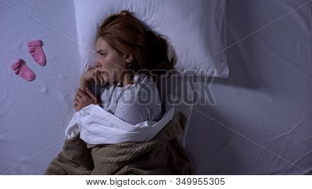Sad Lady Crying Lying In Bed And Looking At Baby Socks Near Pillow, Miscarriage