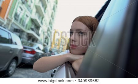 Sad Girl Saying Good Bye To Native City Sitting On Back Seat Of Car, Relocation