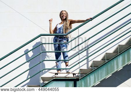 Beautiful Young Black Woman On An Urban Staircase, With Colourful Braids. Typical African Hairstyle.