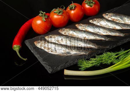Sprat With Vegetables On A Serving Black Board. Small Salted Fish With Onions And Tomatoes. Deliciou