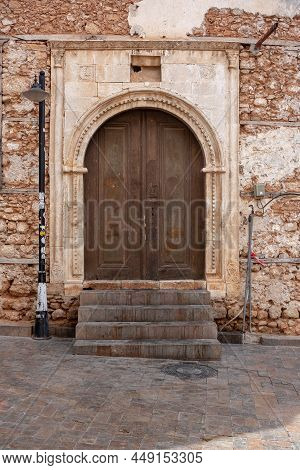 Old Door With Lattice Is Closed By Chain With Lock In Old Stone Wall. Vertical Photo.
