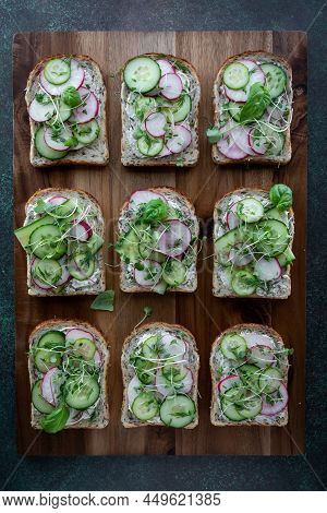 Top Down View Of Cucumber And Radish Open Faced Sandwiches On A Wooden Board.