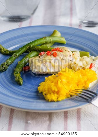 White Fish With Saffron Rice And Some Cheese On Top And Aspargus On The Side