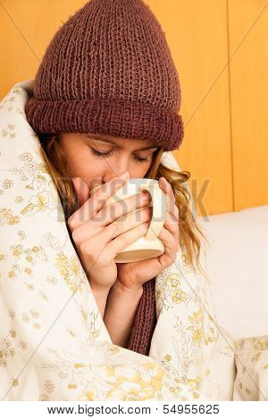 Ill Woman With Feaver Drinking Cup Of Warm Tea Under Blanket