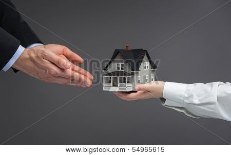 Close up of hands giving home model to other hands. Concept of realty and deal