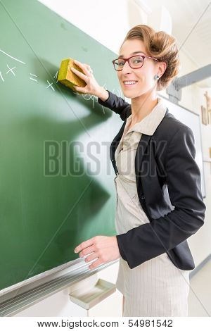 Teacher or docent cleaning the chalk of the board or  chalkboard or blackboard after the math lesson in school class