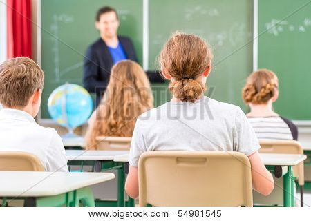 Teacher or educator or docent standing while lesson  in front of a blackboard and educate or teach students or pupils or mates in a school or class