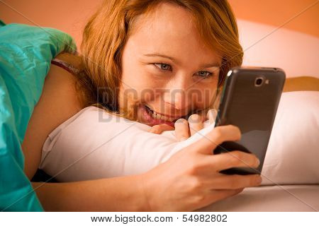 Preety Woman Reading A Sms On Cell Phone In Bed