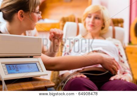 Midwife examining belly of pregnant woman with CTG scanning in practice