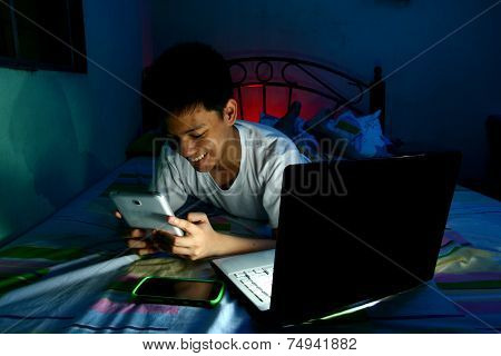 Young Teen in front of a laptop computer and on a bed and using a tablet