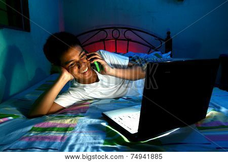 Young Teen in front of a laptop computer and on a bed and using a cellphone or smartphone