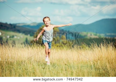 happy little girl runs through a beautiful meadow in the mountains.