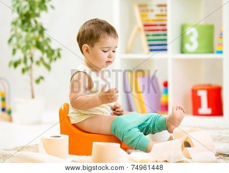 smiling baby sitting on chamber pot with toilet paper
