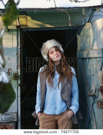 autumn portrait photo of beautiful cold girl wearing fur hat and leather coat standing in doorway