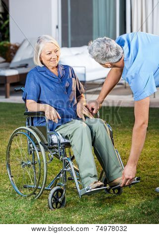Male nurse adjusting footrest for senior woman on wheelchair in lawn at nursing home