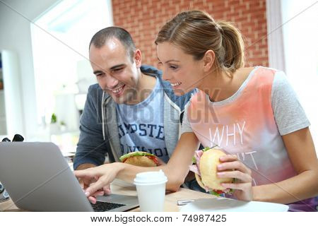 Roommates eating sandwich in front of laptop
